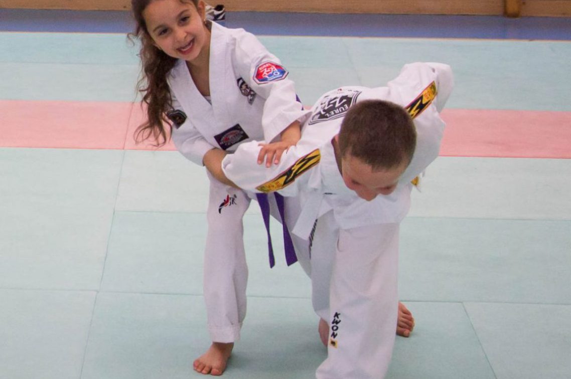 une petite fille pratique de l'autodefense sur un petit garcon au taekwondo